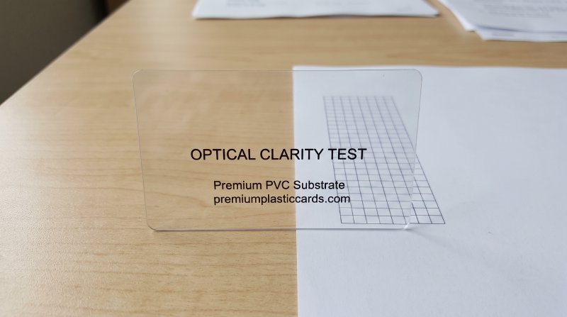 Macro photograph showing a crystal clear 30mil PVC business card over background text demonstrating optical transparency
